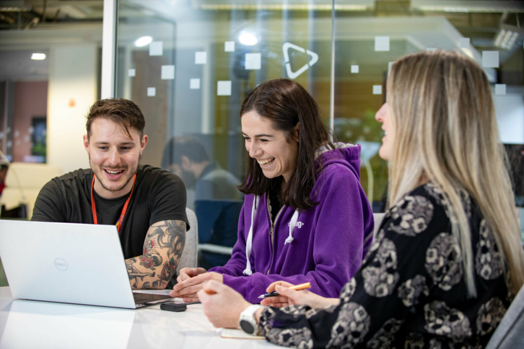 Three people sitting at desk looking at a laptop smiling