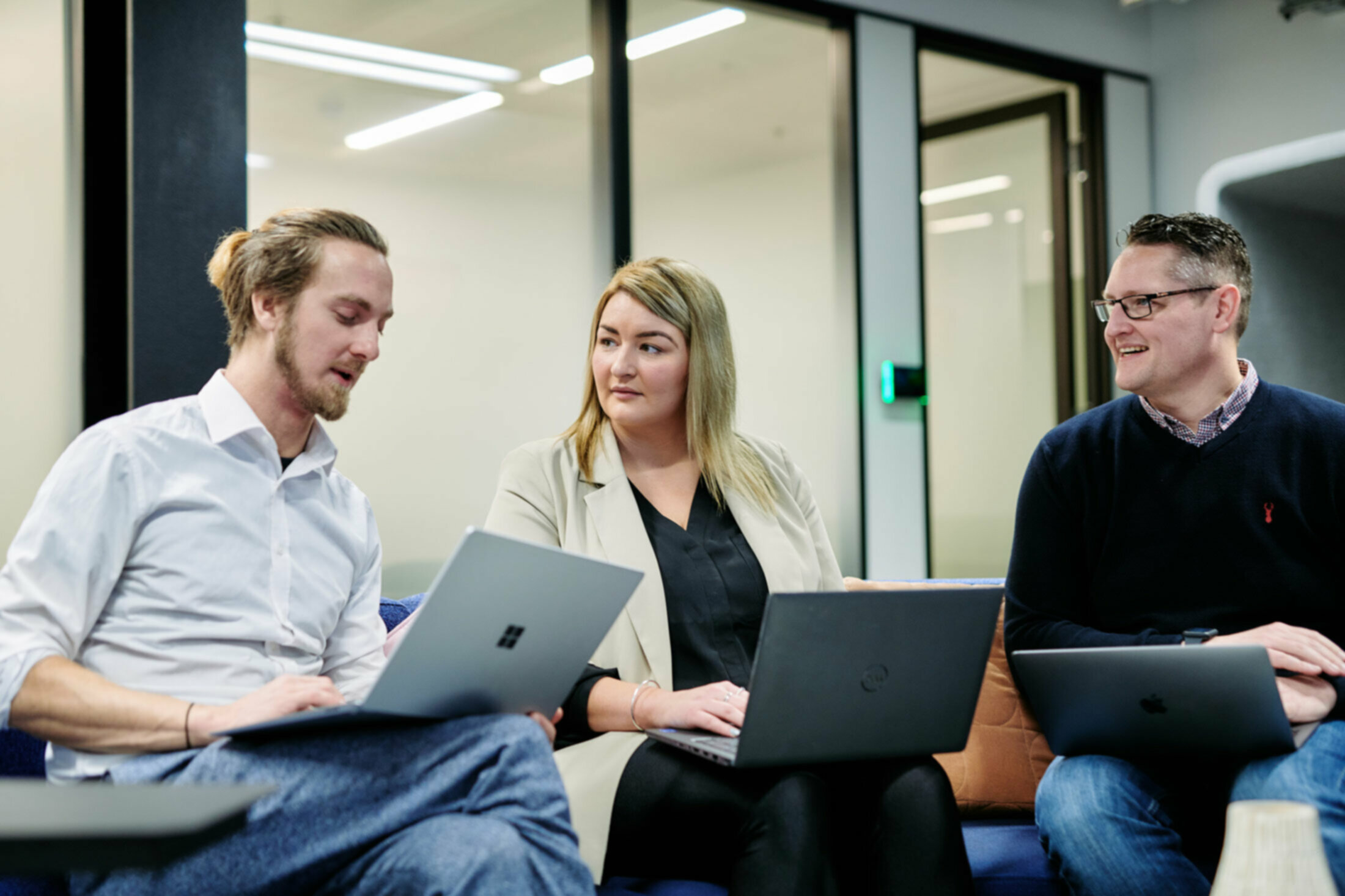 Three people sitting in office with laptops on their laps