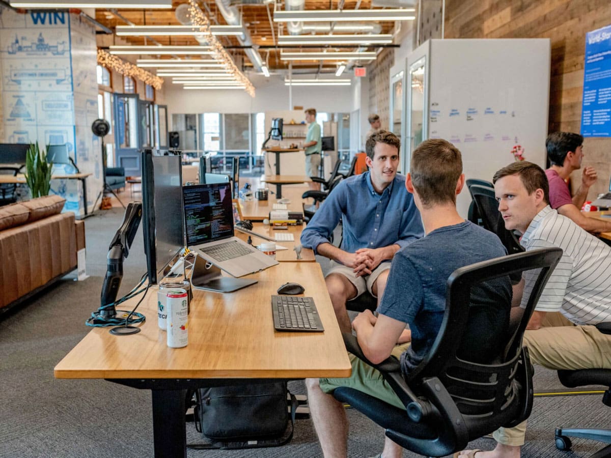 Three men sitting around a desk in an office talking