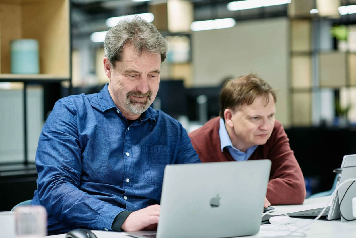 Two men sitting at a desk looking at laptops