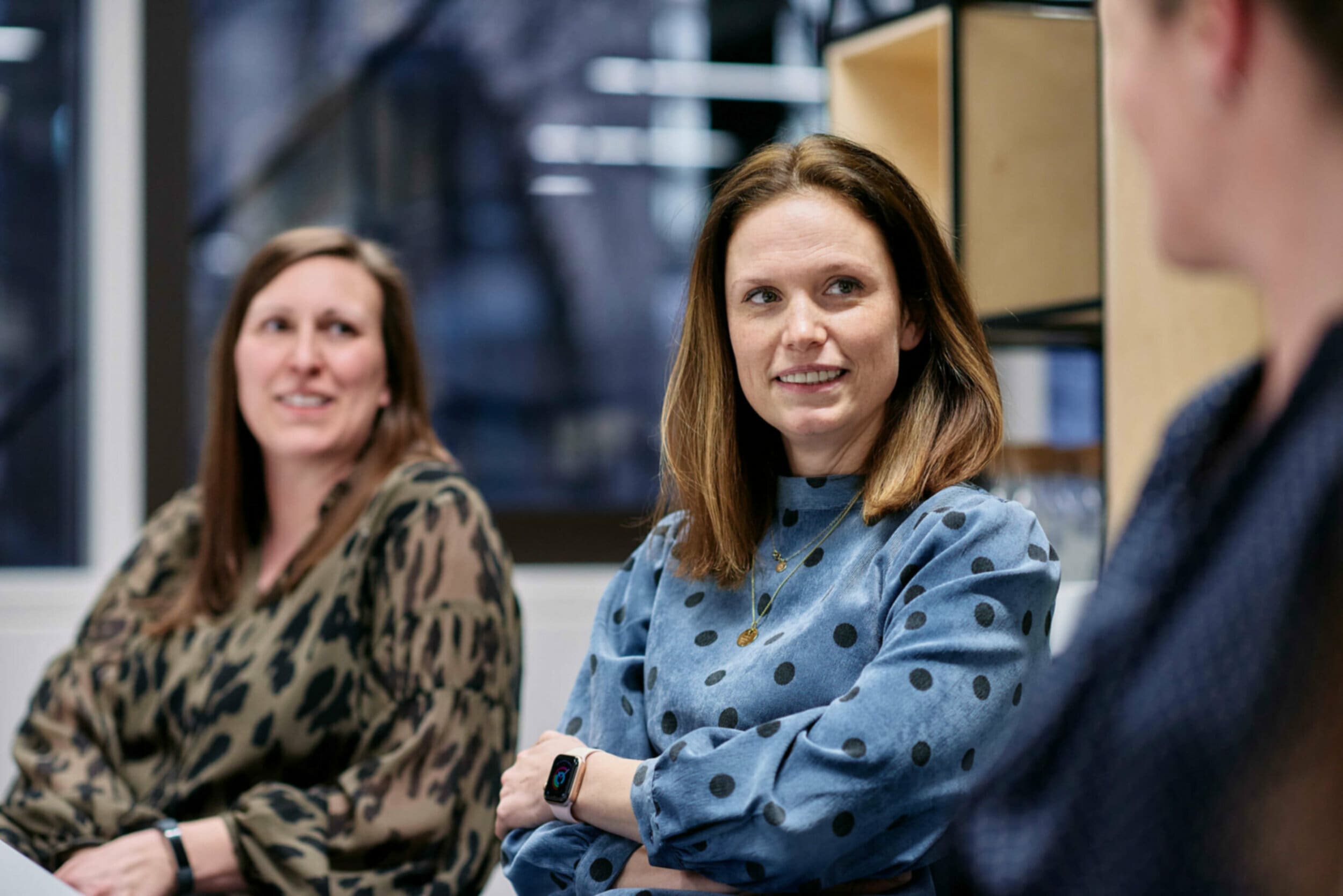 Two women sitting at office desk listening to coworker