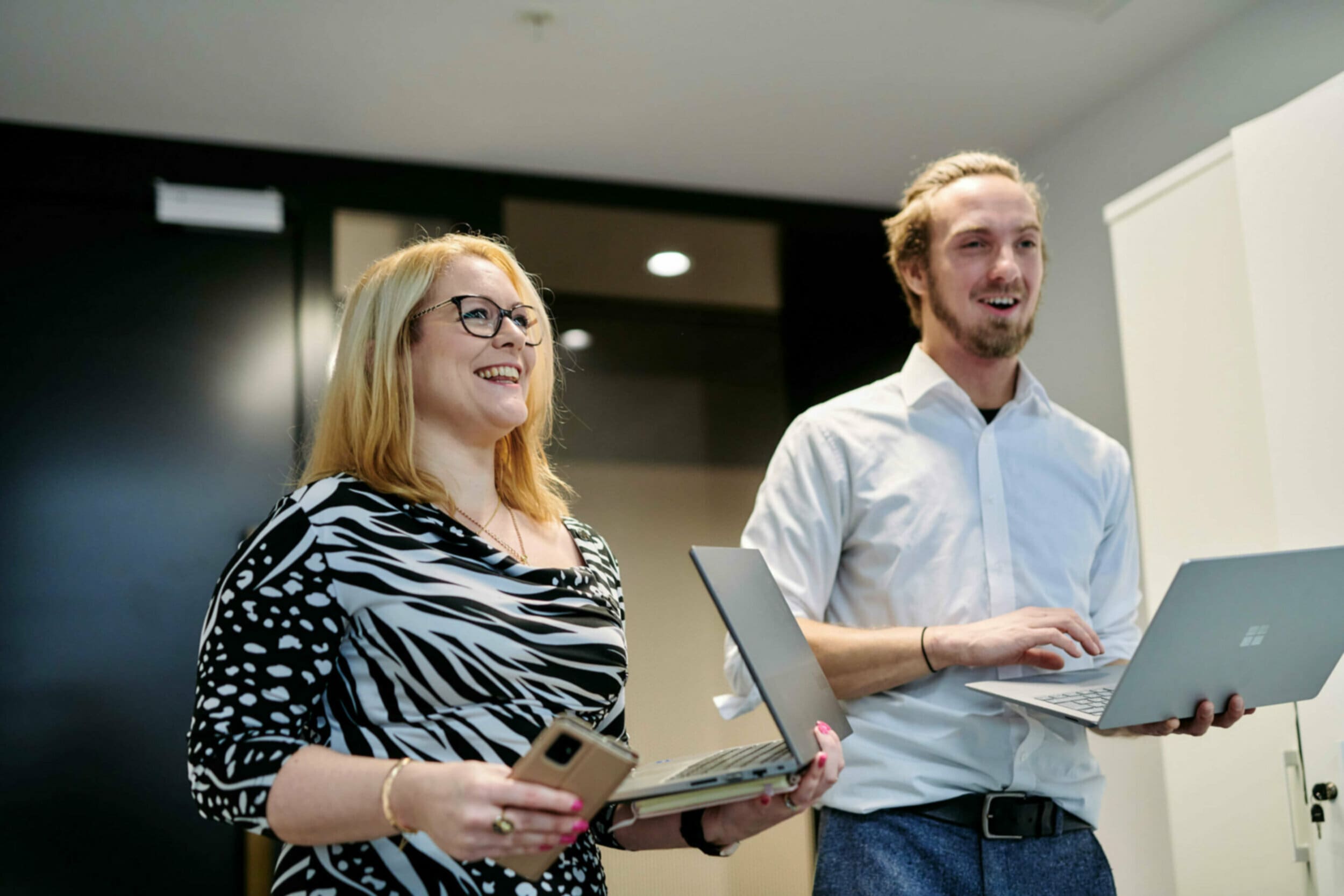 Man and woman holding laptops walking in the office