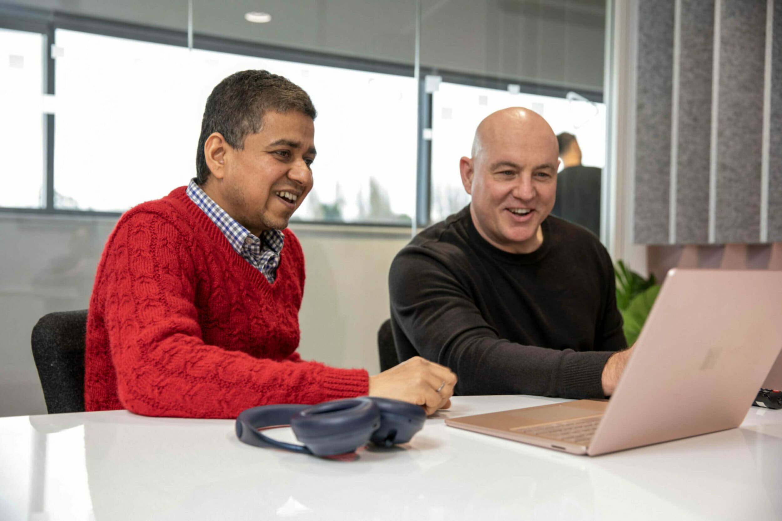 Two men smiling at a laptop on a desk