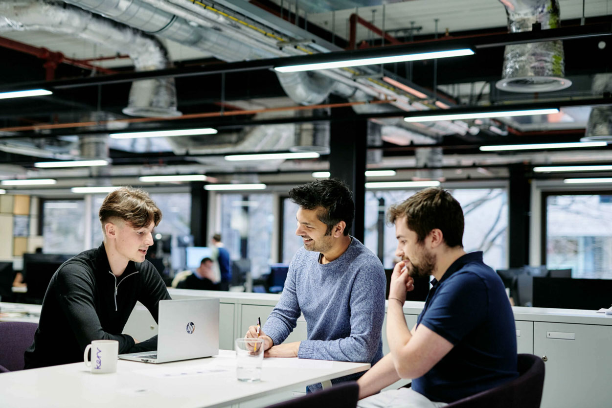 Three men sitting at a desk in an office