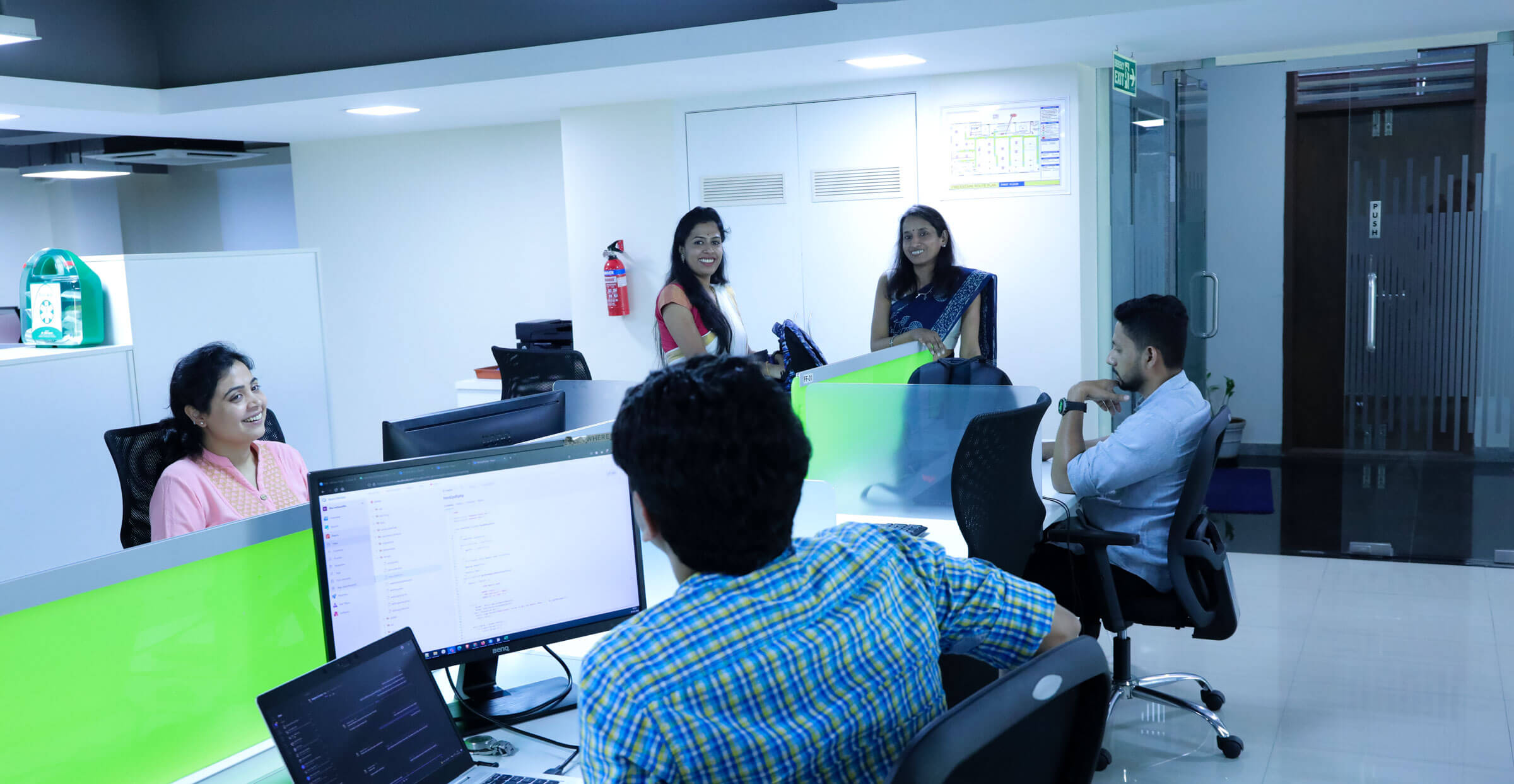 Multiple people standing around office computer desks