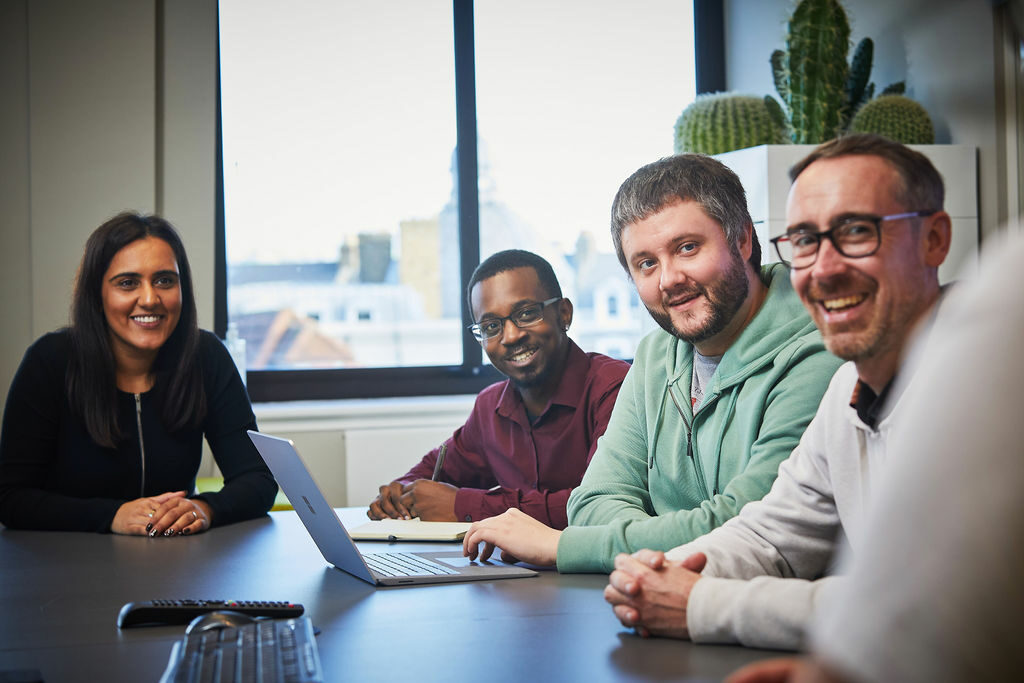 Four people sitting at desk smiling