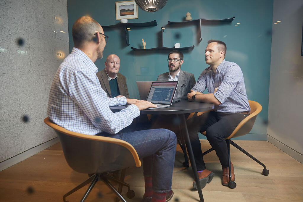 Four men sitting around a table with laptops in an office