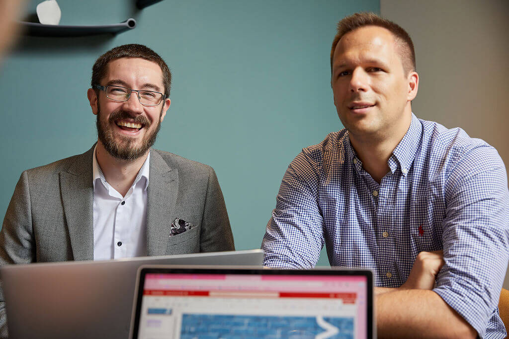 Two men smiling at camera sitting with laptops