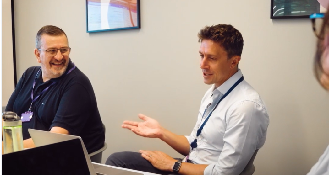 Man sitting at desk with coworkers talking