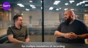 Two men talking at a table with the Kerv logo in the corner