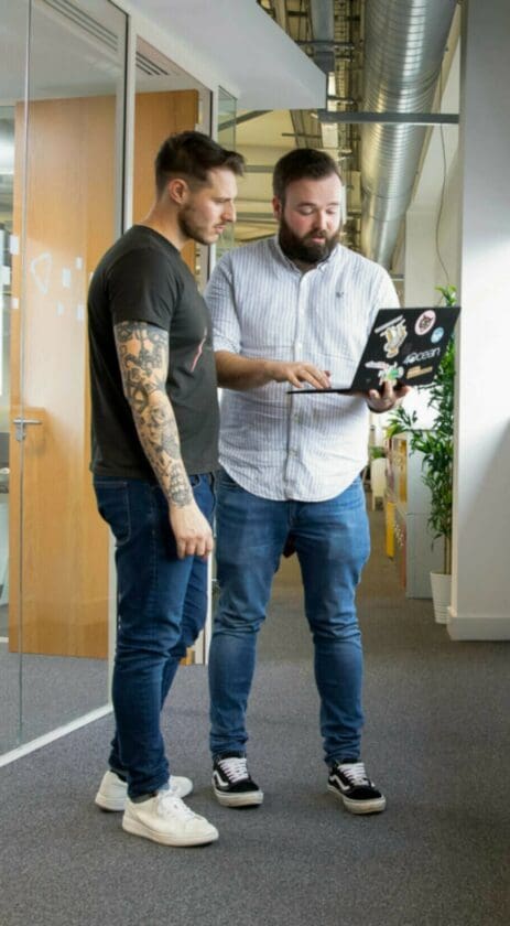 two-men-in-office-corridor-holding-laptop