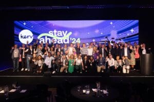 Group of people standing on stage with 'Stay Ahead' banner in the background