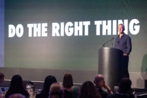 Man standing at podium in front of screen saying 'Do the Right Thing'